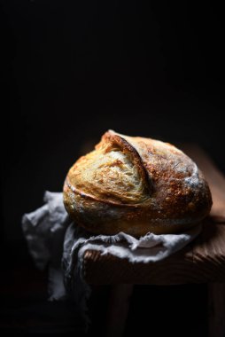 Kırık kabuklu ve kaba ahşap bir masada sert desenli iştah açıcı ekşi ekmek. Zanaatkar çiftlik tarzı somun somun sıcak doğal ışıkla yakalanır.