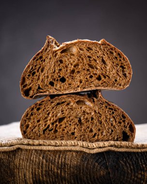 Rustik ahşap bir tahtanın üzerinde iki parça çavdar ekmeği. Zanaatkar çiftlik tarzı somun somun sıcak doğal ışıkla yakalanır.