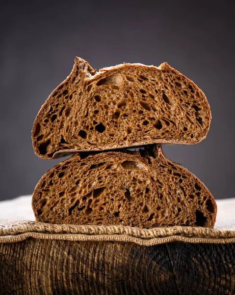 Rustik ahşap bir tahtanın üzerinde iki parça çavdar ekmeği. Zanaatkar çiftlik tarzı somun somun sıcak doğal ışıkla yakalanır.