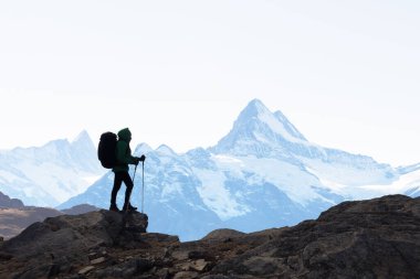 Karlı dağlara karşı duran bir sırt çantasının silueti. Seyahat ve macera konsepti