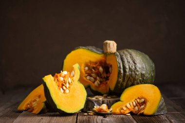 Dilimlenmiş yeşil balkabağı ve parlak turuncu et bir bıçağın yanında, tahta tahtada oturuyor. Sonbahar yemek sahnesi Şükran Günü hazırlığı ya da Cadılar Bayramı hasat dekoru için mükemmel.