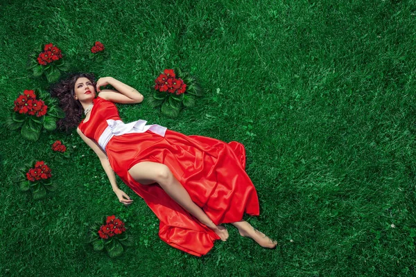 草の上に横たわる赤いドレスの若い女性の穏やかな印象は パーソナライズされたテキストやオブジェクトのための十分なスペースを提供します — ストック写真