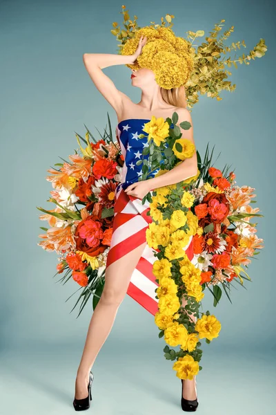 愛国的なアメリカの国旗で飾られたドレスを着た若い女性の全長の肖像画 中立的な背景に撮影されたこのスタジオは 愛国心と花のエレガンスの両方を抱く女性の美しさを捉え 7月4日にぴったりです — ストック写真