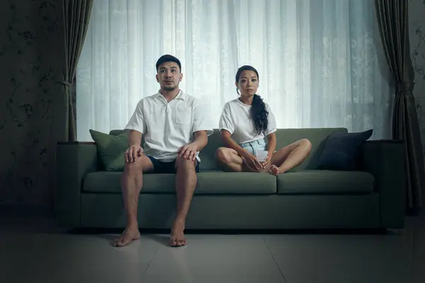 一对年轻夫妇穿着随意地坐在客厅的一张绿色沙发上 背靠着窗帘 沉思地凝视着 — 图库照片