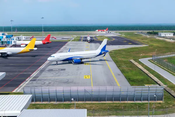 A busy airport tarmac runway with various commercial aircraft planes parked near the terminals, surrounded by airport buildings, structures, and facilities.