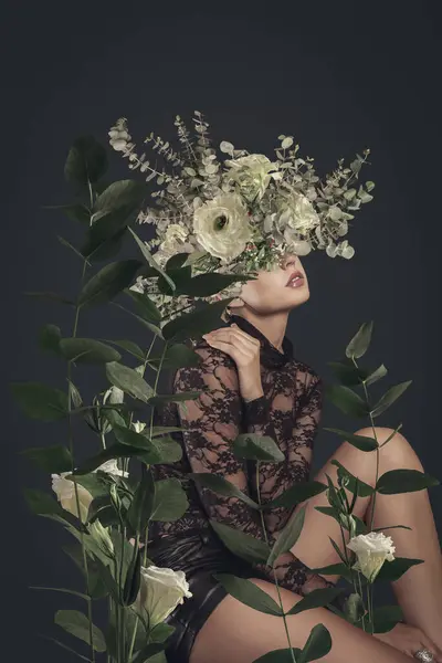 フローラルなヘッドドレスを持つ官能的な女性は 芸術的な植物の肖像画で緑豊かな葉と花の間にポーズします ロイヤリティフリーのストック写真
