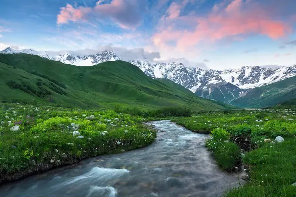 Geniş nehir akıntısının panoramik manzarası renkli taşlarla dolu. Beyaz kar tepeleri, yeşil çayırlar ve bulutlu gökyüzü olan dağlar. Buzullu bir fotoğraf. Yukarı Svaneti, Gürcistan, Avrupa. Mutlu bir yaşam tarzı. Güzel evren.