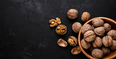Walnuts in a wooden plate and scattered on a black background. Place for text
