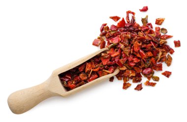 Kırmızı biber taneleri beyaz arka planda yakın plan ahşap bir kepçeden döküldü. Ezilmiş biber görünümlü üst