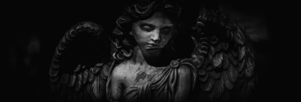 Black and white horizontal image of sad angel of death. Fragment of an ancient statue.
