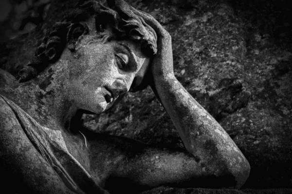 Very ancient stone statue of man crying on the tomb for the loss family. Death, cemetery, end of human life.