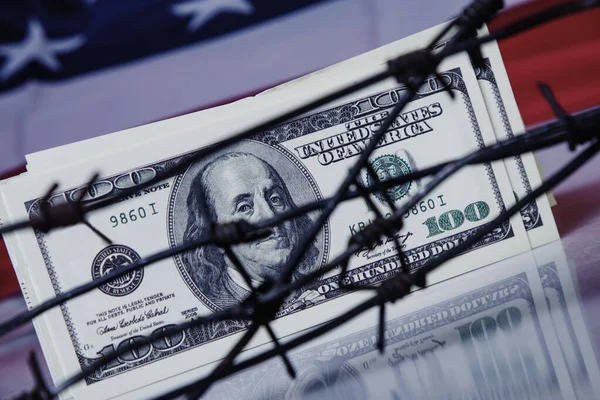 stock image Close up US Dollar money wrapped in barbed wire against United States national flag as symbol of economic warfare, sanctions and embargo bustin