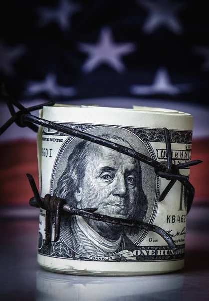 stock image Rolled American Dollars banknotes wrapped in barbed wire against United States national flag as symbol of economic warfare, sanctions and embargo busting
