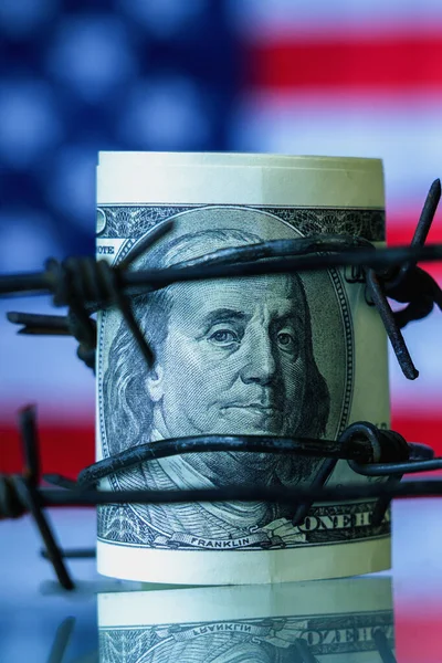 stock image US Dollar currency wrapped in barbed wire against flag of United States as symbol of economic warfare, sanctions and embargo busting concept. Vertical image.