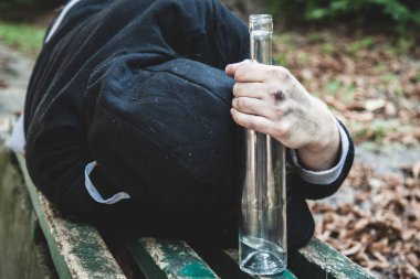 Addiction and Inner Emptiness: psychological problems of people. Antisocial behavior of a young man escapes reality and life's unlived difficulties. Alcogol addiction man lying outdoors on bench. Horizontal image.