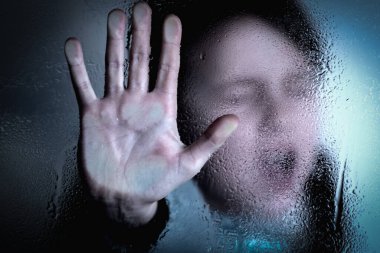 Violence, abuse, school bullying, body language concept. Portrait of beautiful female kid standing behind wet glass  and doing stop gesture.