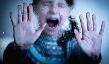 Protect children and young underage people from violence, exploitation, abuse, and neglect concept. Young girl screams and making STOP gesture behind wet glass. Horizontal image.