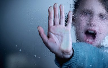 Conceptual image: Protect children and young underage people from violence, exploitation, abuse, and neglect. Young girl showing stop gesture from behind wet glass. Copy space.