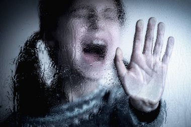 Violence, abuse, school bullying, body language concept. Dramatic portrait of beautiful female kid standing behind wet glass  and doing stop gesture.