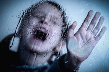 Scared young girl making NO sign, showing hand STOP gesture. Kid standing behind wet glass and says No to domestic violence, abuse, school bullying,  problem concept