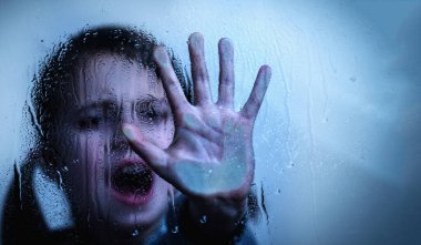 Young girl with a raised hand showing STOP gesture behind wet glass. Copy space for design.