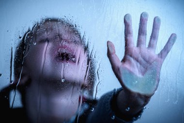 Portrait of young child girl stretch hand and show STOP gesture behind wet glass. Protest against domestic violence, against discrimination or school abuse.