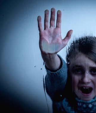 Pain, fear, violence concept. Close up portrait of upset little girl protesting behind wet glass.  Copy space.