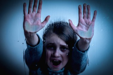Pain, fear, violence concept. Close up portrait of sad upset little girl protesting behind wet glass.  