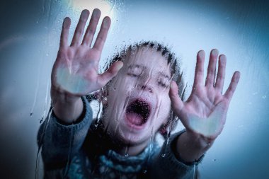 Portrait of up upset little girl protesting behind wet glass. Pain, fear, violence concept.