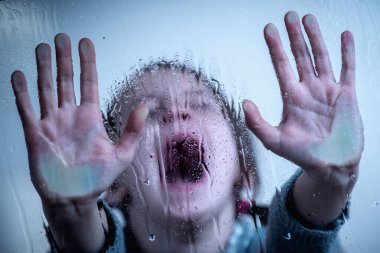 Close up upset little girl protesting behind wet glass. Horizontal image.