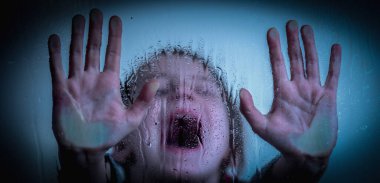 Upset little girl protesting behind wet glass. Horizontal image.