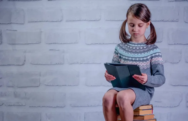 Young girl sitting on stack of books with PC tablet. Concept of learning new knowledge, self improvement and development of mental abilities. Copy space.