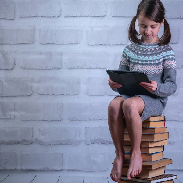 Young girl sitting on stack of books with PC tablet. Concept of learning new knowledge, self improvement and development of mental abilities. Copy space.