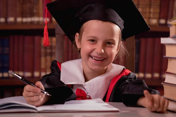 Education, school, knowledge concept. Portrait of happy beautiful child girl  in graduation cap learning in library.