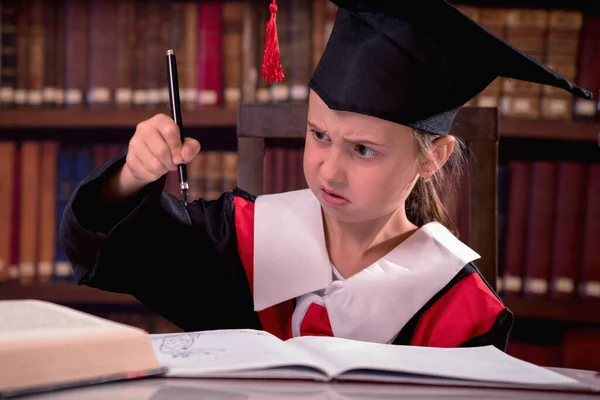 Education, school, knowledge and people concept. Funny portrait of young disappointed girl in graduation cap cannot write and study because the pen stopped working