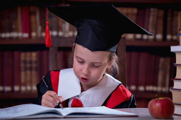 Education, school, knowledge and people concept. Portrait of young beautiful child girl  in graduation cap reading books in library.