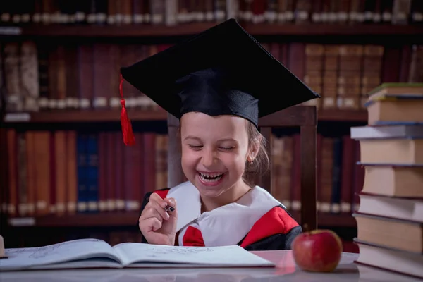 Education, school, knowledge and people concept. Happy beautiful child girl  in graduation cap reading books in library.