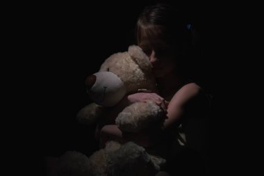 Kavramsal görüntü: Kayıp çocukluk. Üzgün, korkmuş ve yalnız genç bir kızın psikolojik portresi oyuncak ayıyla yan yana otururken terk edilmiş, üzgün, yalnız bir çocuğun oyuncak bebek kucaklaması gibi..