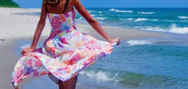 Güneş ışığında deniz kıyısında dans eden, elbise giymiş, güzel, zayıf bir kadın. Tatil, yaz tatili, dinlenme konsepti. Boşluğu kopyala.