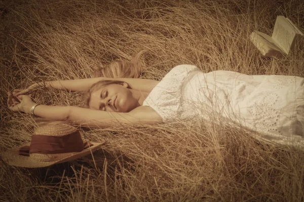 美しい若いですブロンド女性の肖像画は本と乾燥した草の上に黄金の夏のフィールドにあります — ストック写真