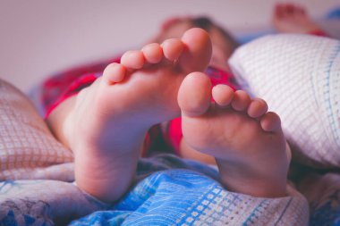 Küçük kız evde yatakta uyuyor. Ayakları yatak odasındaki battaniyenin altında. Tatil, uyku ve rahatlama konsepti. Yatay resim.