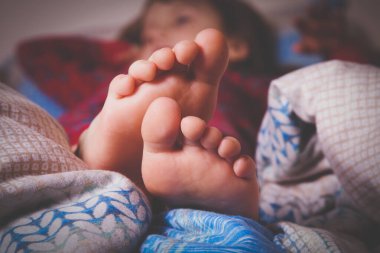 Küçük bir kızın yataktaki görüntüsü. Uykunun sembolü olarak ayaklarını battaniyeye sar ve rahatla. Yatay resim.