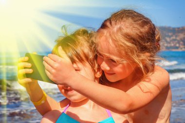 Yaz tatili ve eğlence konsepti. En iyi iki arkadaş, şirin kız çocuklar, deniz kıyısındaki akıllı telefonlarda selfie çekiyorlar..