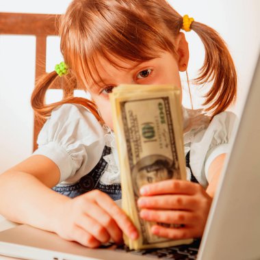 Mutlu iş kızı uzaktan çalışıyor, dizüstü bilgisayar kullanıyor ve Amerikan dolarlarını sayıyor. Mobil sistem konseptinde iş yapmak. Gözlere seçici odaklanma.