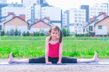 Genç sportif çekici kız ısınma egzersizi yapıyor ve bacaklarını açıyor. Açık havada çalışıyor. Kentsel koşullarda spor eğitimi.
