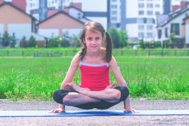 Mavi minder üzerinde yoga yapan genç ve çekici bir kız bacak bacak bacak üstüne atarak kol dengesi egzersizi, duruş şekli, Tolasana, Utpluthi Poz, tam boy.