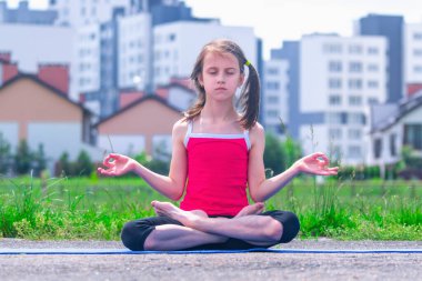 Yoga nilüferinde oturan çekici genç bir kızın portresi, şehrin süper hızlı temposundaki sağduyu ve zihin huzurunun korunmasının sembolü olarak şehir arka planında poz veriyor.