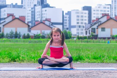 Mavi hasırda yoga yapan genç ve çekici bir kızın portresi bacak bacak bacak üstüne atarak kol dengesi egzersizi, Pul Duruşu, Tolasana, Utpluthi Poz, tam boy.