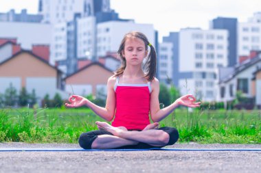 Yoga nilüferinde oturan çekici genç kız şehrin arka planında huzur ve dengenin korunmasının sembolü olarak poz veriyor.