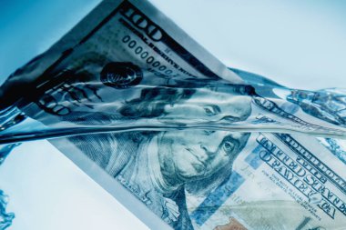 Küresel mali krizin ve uluslararası ticaret ve yatırımın belirsiz geleceğinin simgesi olarak suya batan Amerikan Doları banknotlarını kapatın. Seçici odaklanma. Yatay resim.